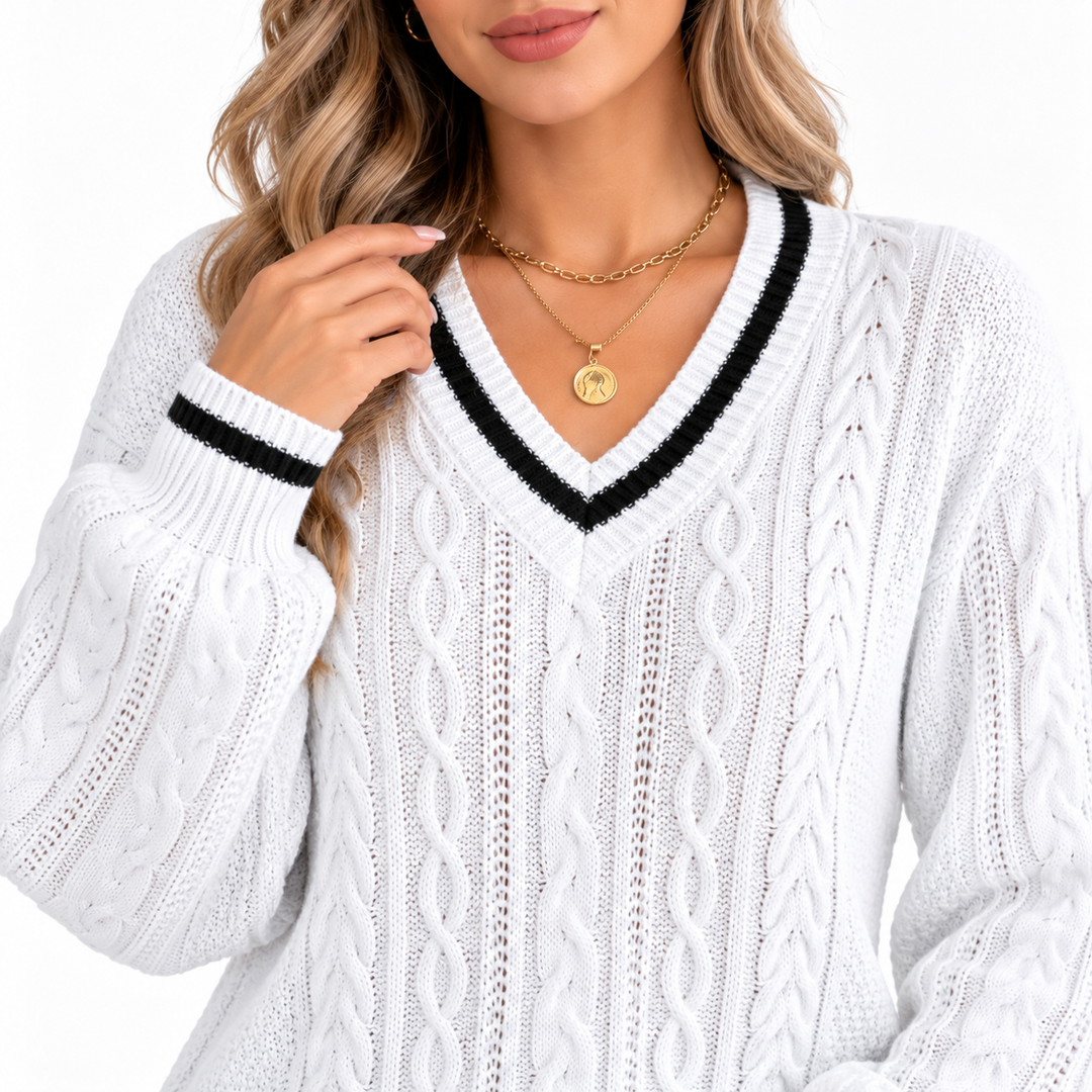 Close view of white cable knit V neck sweater showing black trim, textured knit panels and ribbed cuff detail on a model