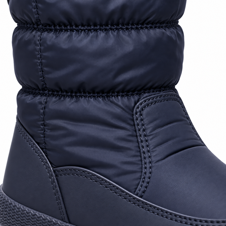 Close-up of a navy winter boot showing padded shaft texture, stitched panels and the lower upper construction in studio detail.