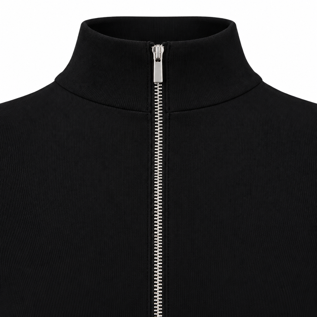 Close detail of a black jumpsuit with stand collar and silver front zipper, fully fastened against a white studio background.