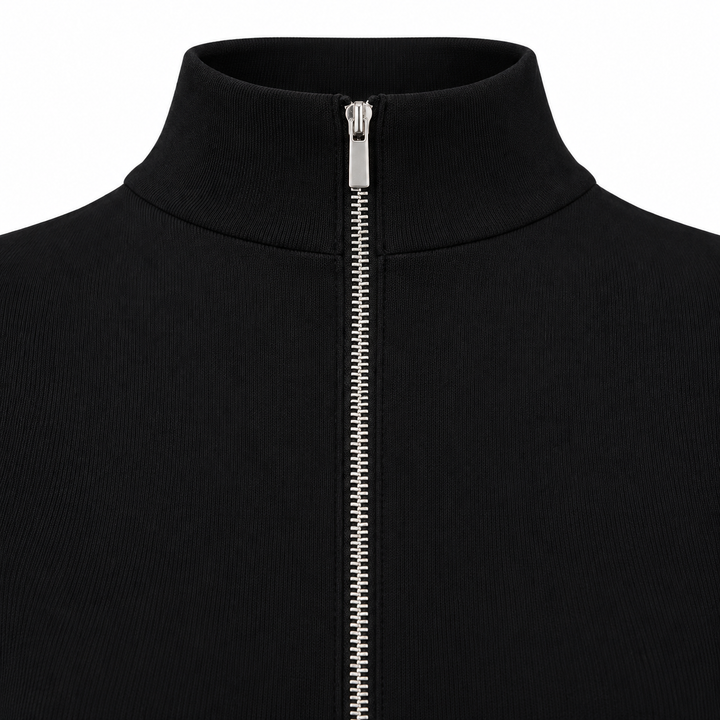 Close detail of a black jumpsuit with stand collar and silver front zipper, fully fastened against a white studio background.